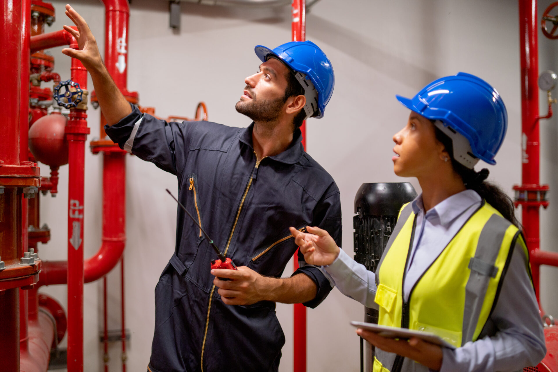 Two engineer or technician worker discuss about red pipe system in the construction site to maintenence and fix the problem together.