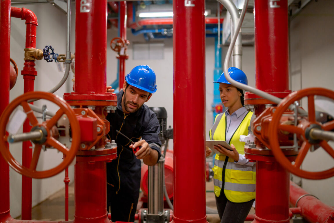 Two engineer or technician worker discuss about red pipe system in the construction site to maintenance and fix the problem together.